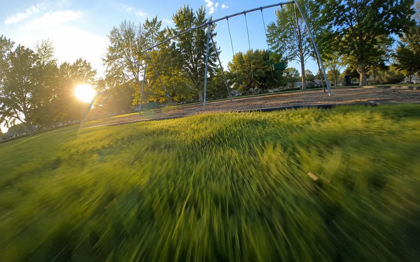 POV frame at toddler height running toward the swing set, grass motion-blurred